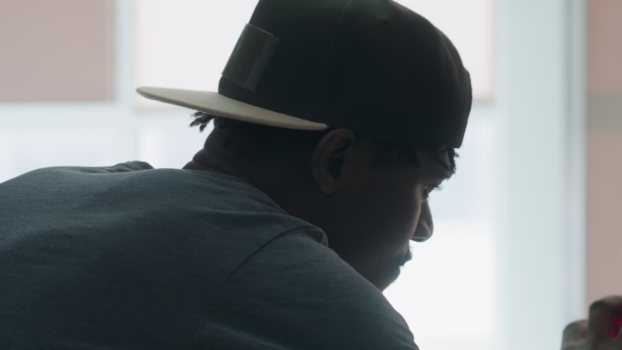 close up of young student in cap reaching arm forward while searching through bookshelves in bright library interior with focused expression and soft light