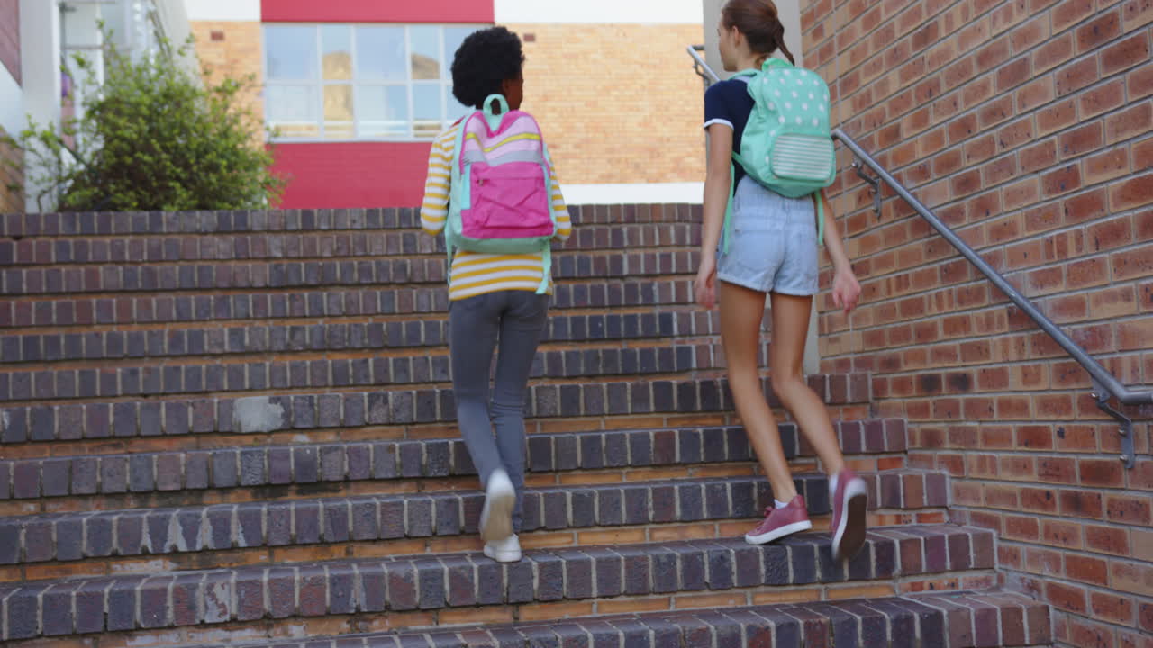 Walking up stairs, two girls with backpacks heading to school building, copy space