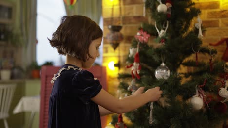 Little-girl-in-dress-decorating-Christmas-tree-at-home