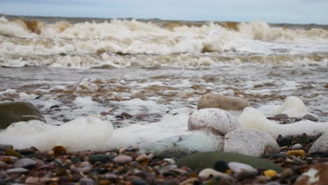 Foamy-breaking-ocean-surf-pebble-beach-shoreline-tide-soothing-multicoloured-stones