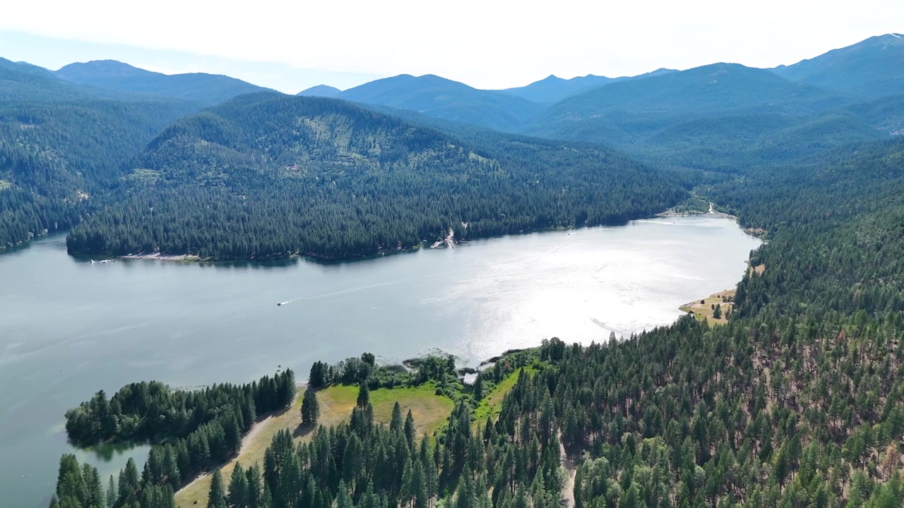 Betagende luftfoto-panorama der viser en uberørt blå sø placeret i en stor grøn fyrreskov under strålende sommersol i Californien, USA