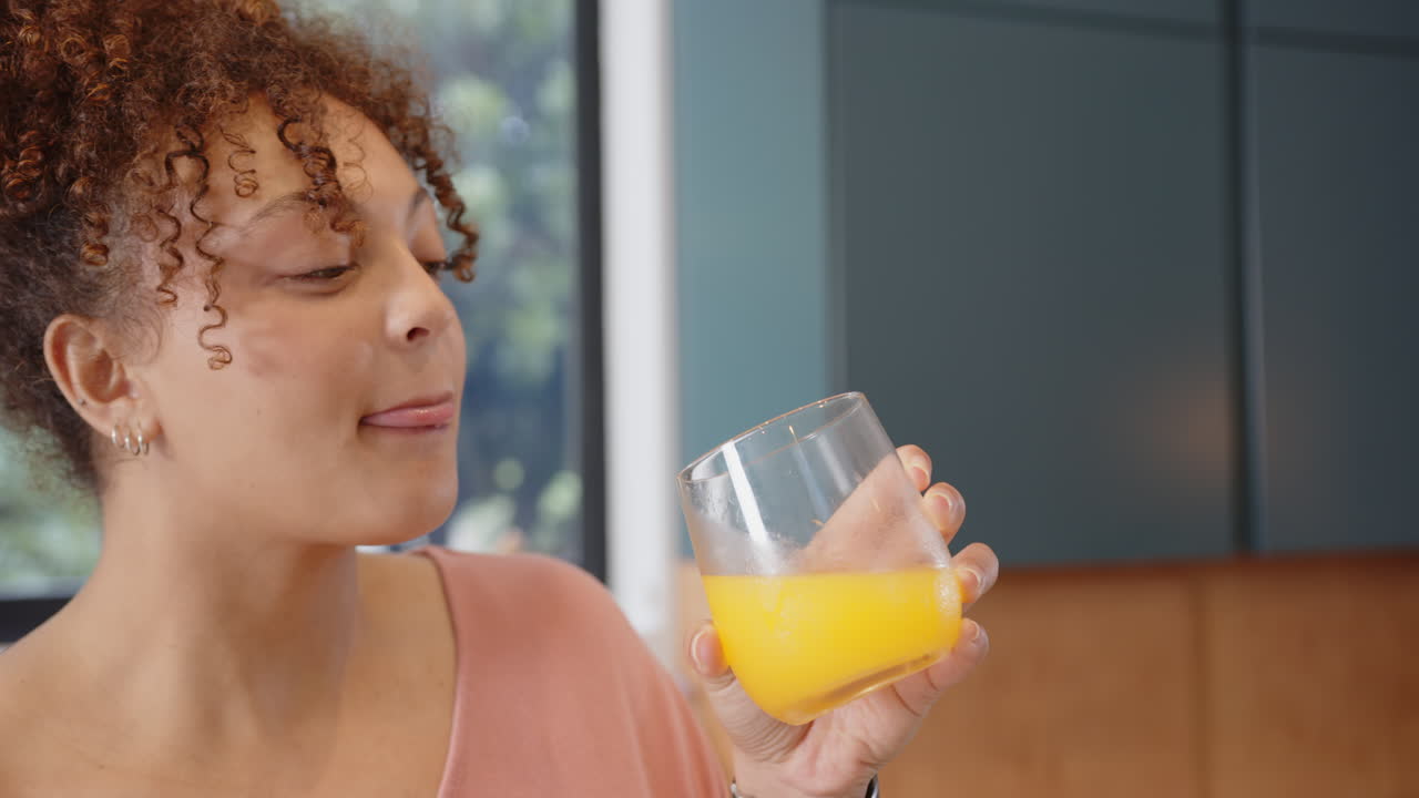 Drinking orange juice, plus size woman enjoying healthy refreshment in kitchen