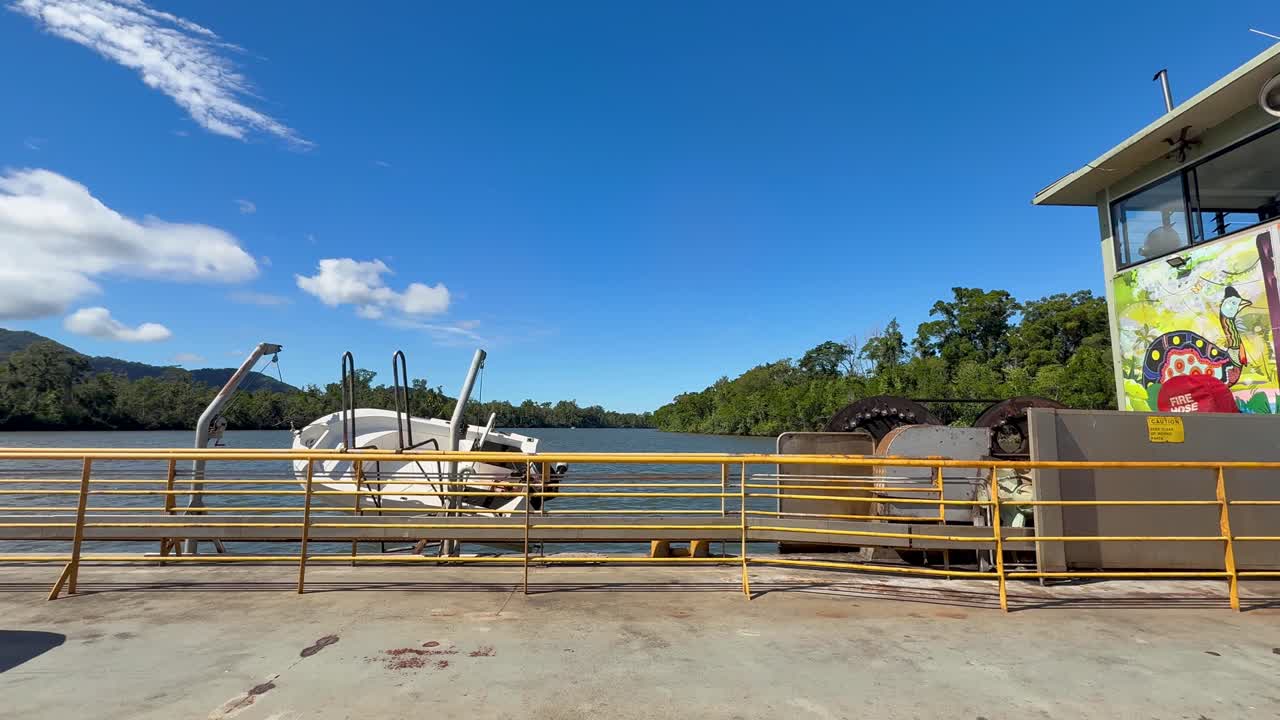 Ferry transports vehicles across wide river under bright daylight, surrounded by lush tropical landscape