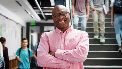 portrait of male high school teacher standing by stairs in busy college building