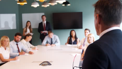 pull focus shot of mature businessman addressing group meeting around table at graduate recruitment assessment day