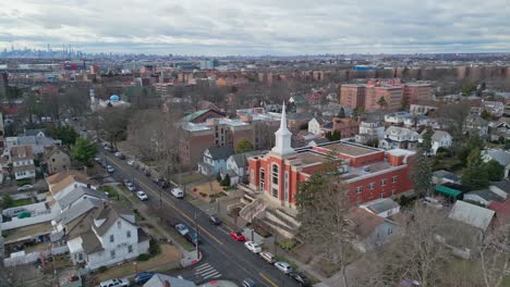 Aerial-orbiting-shot-of-church-in-Queens-District-with-skyline-of-Manhattan-in-background-during-cloudy-day