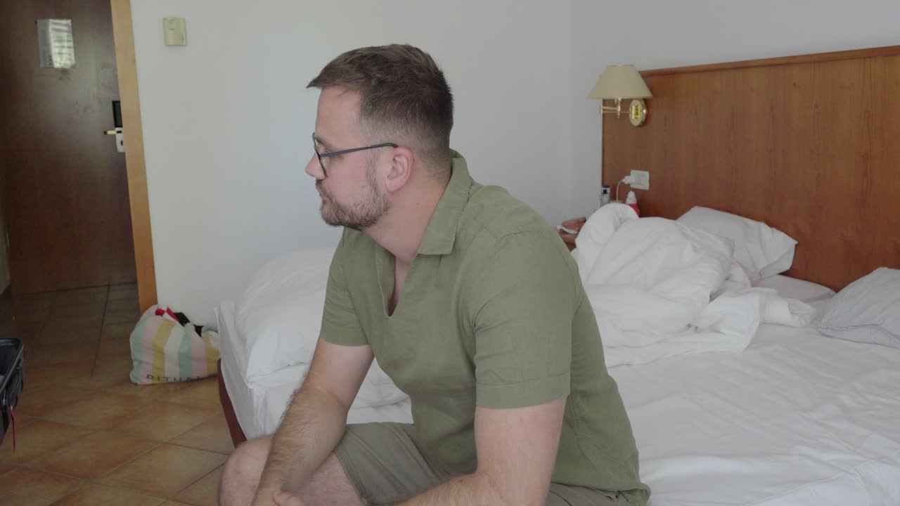 A man in a hotel room angrily throws his laptop onto the bed. His posture and expression reflect failure, frustration, stress, or feelings of depression