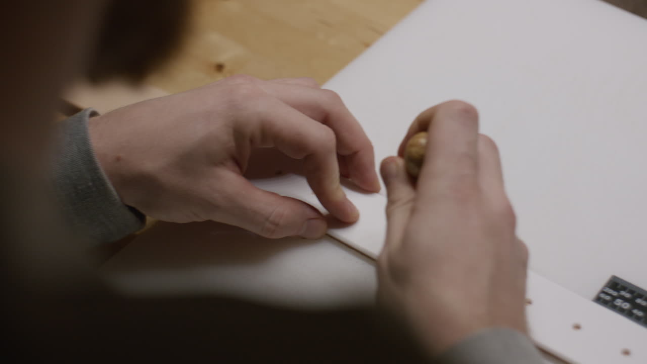 A craftsman carefully uses an awl to puncture stitching holes on a leather strap, ensuring precision in leathercraft.