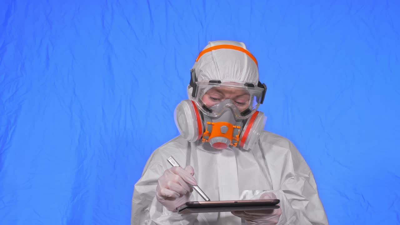 científico virólogo en respirador hace escribir en una tableta con lápiz. mujer con máscara médica de protección. clave de croma azul.