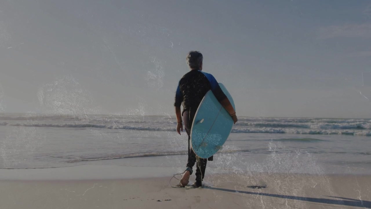 Surfista donna anziana che scruta l'orizzonte, sistema la tavola da surf sotto il braccio ed entra tra le onde per fare sport.
