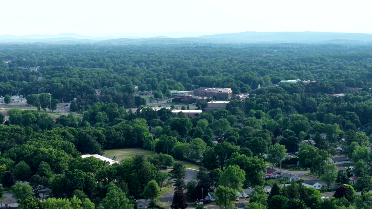 Drone lentää eteenpäin Western New England Universityn kampuksen yllä, jota ympäröi tiheä vihreä puusto, vuorijono taustalla Longmeadow'ssa, Massachusettsissa.