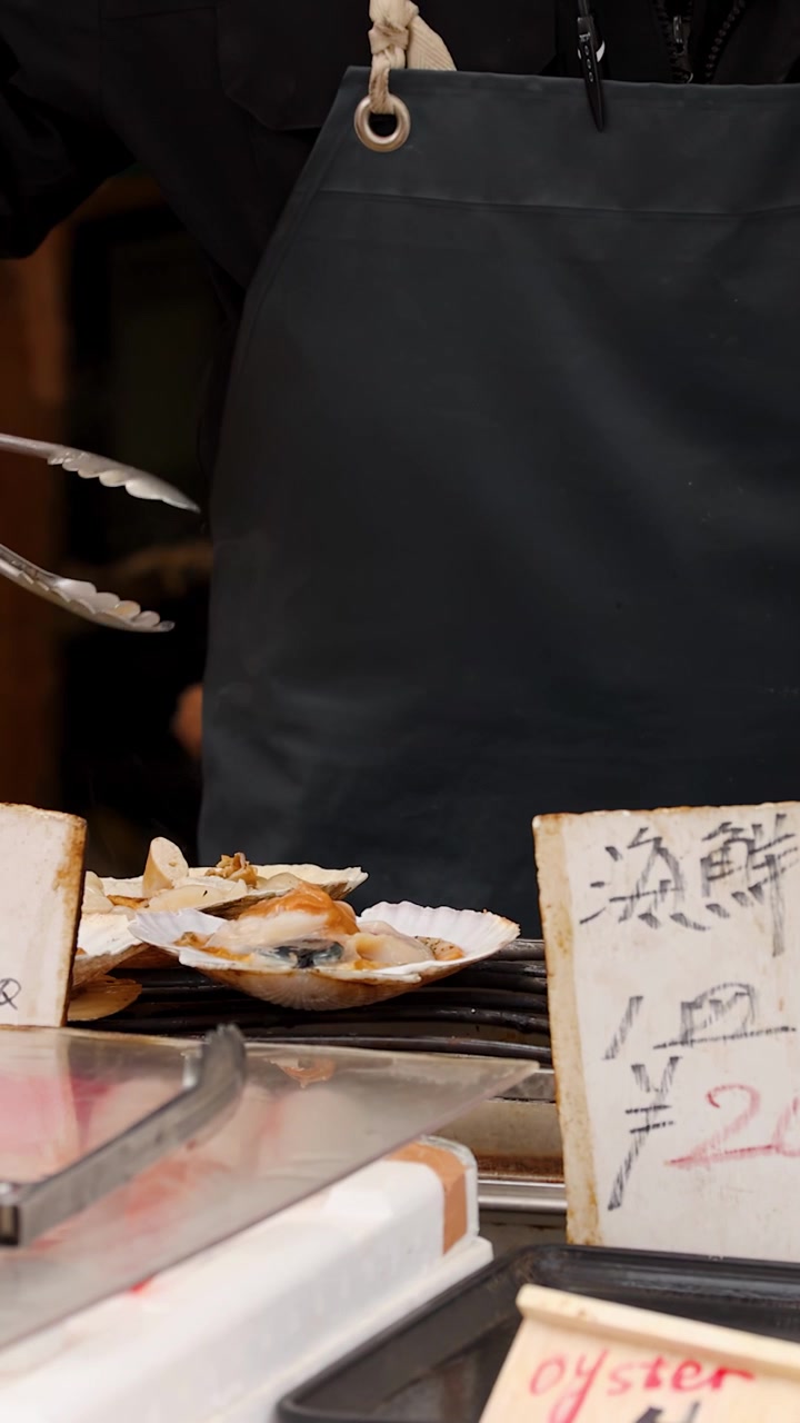 Uno chef usa le pinze per grigliare capesante fresche al mercato del pesce di Tsukiji a Tokyo