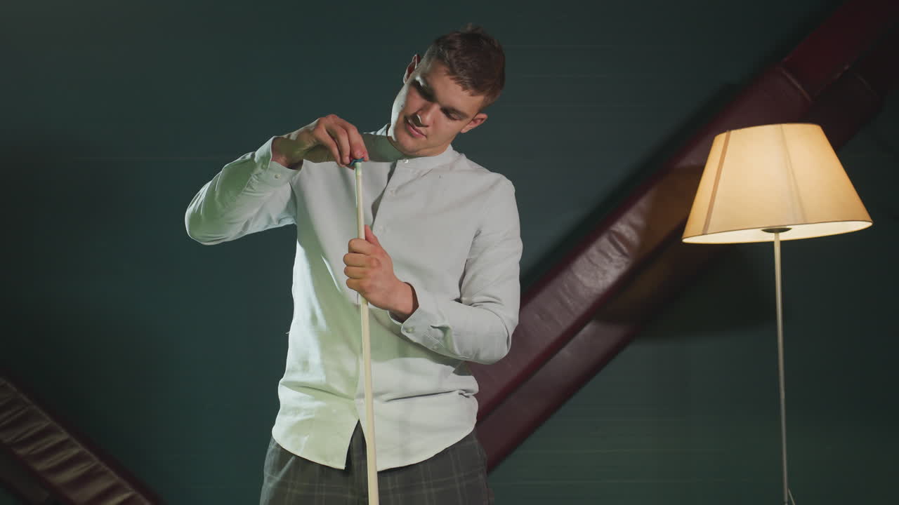 парень в белой рубашке и серых брюках держит палку, нанося красную крышку, улыбаясь. темный фон и теплое освещение создают сосредоточенную, но расслабленную атмосферу, подчеркивая точность