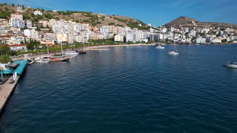 Escena-Pintoresca-De-La-Bahía-De-La-Ciudad-Costera-De-Saranda-Con-Muelle,-Paseo-Marítimo,-Hoteles,-Destino-Turístico-Junto-Al-Mar-Azul-Profundo