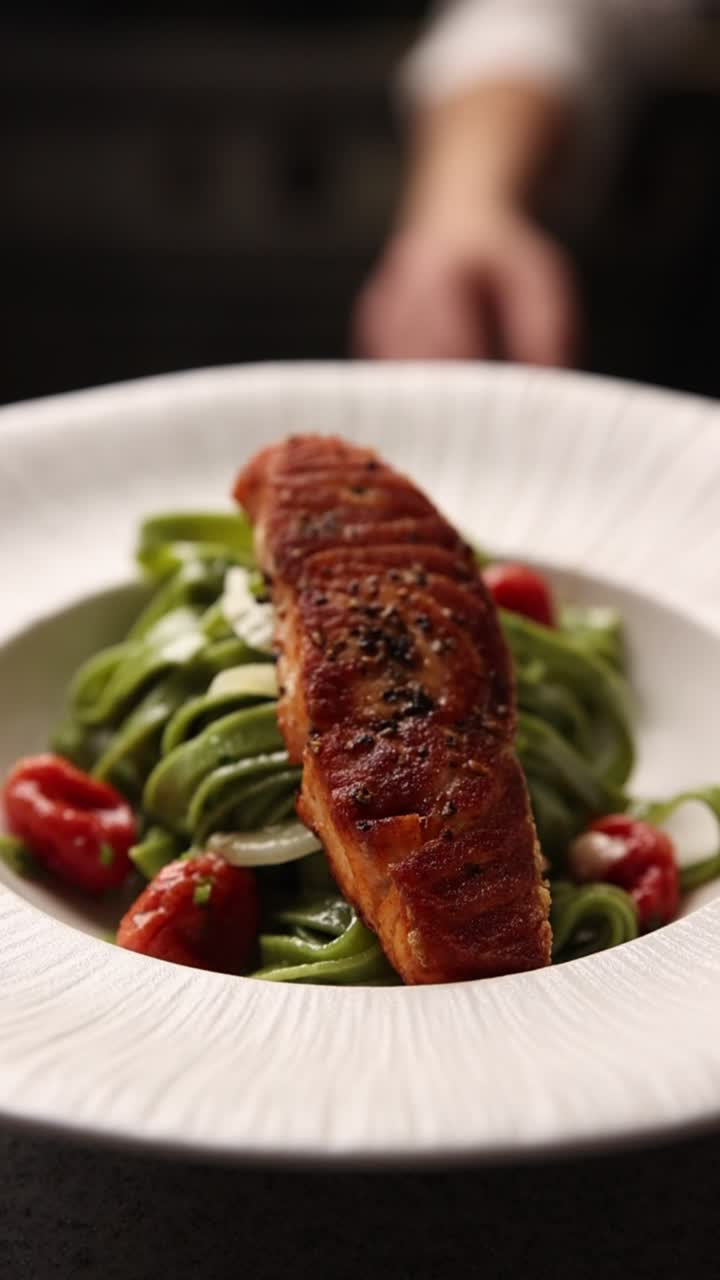 Chef che impiattano filetti di salmone su pasta verde con pomodorini