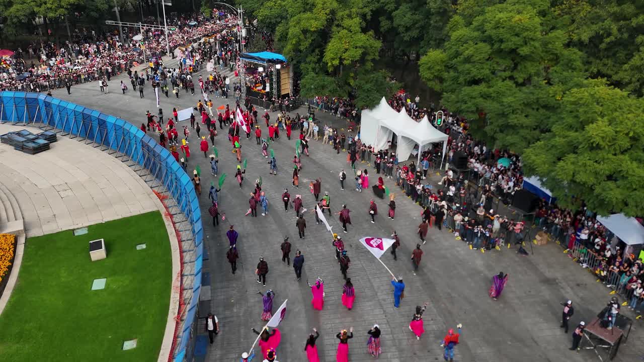 Aerial shot of participants in the Day of the Dead parade with colorful banners over Paseo de la Reforma in Mexico City