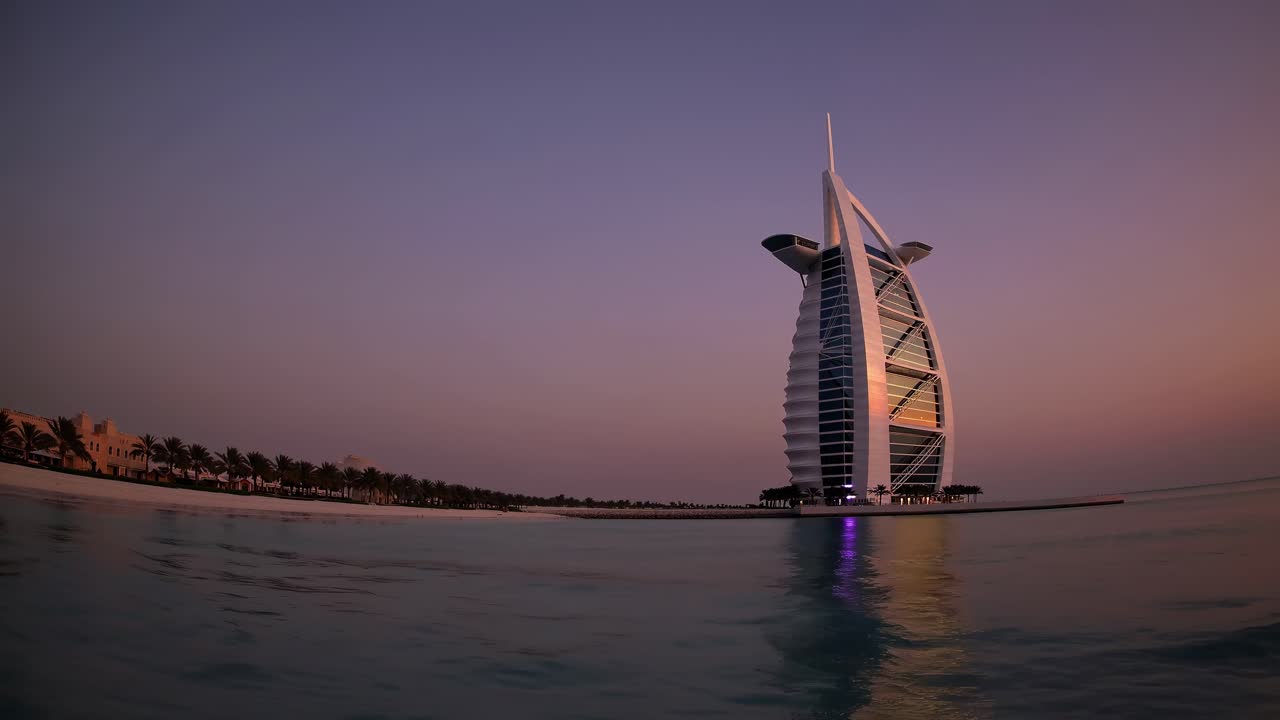 Scenic view of the Burj Al Arab, a luxury hotel located in Dubai, United Arab Emirates, reflecting on the calm sea during a breathtaking sunset, creating a tranquil and picturesque scene