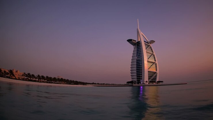 Scenic view of the Burj Al Arab, a luxury hotel located in Dubai, United Arab Emirates, reflecting on the calm sea during a breathtaking sunset, creating a tranquil and picturesque scene