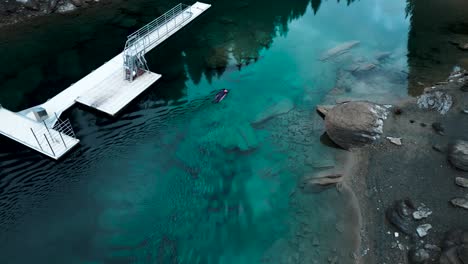 Vista-Aérea-De-Un-Hombre-En-Un-Neopreno-Nadando-En-Una-Tabla-En-Un-Prístino-Lago-De-Agua-Azul-Caumasee-En-Suiza