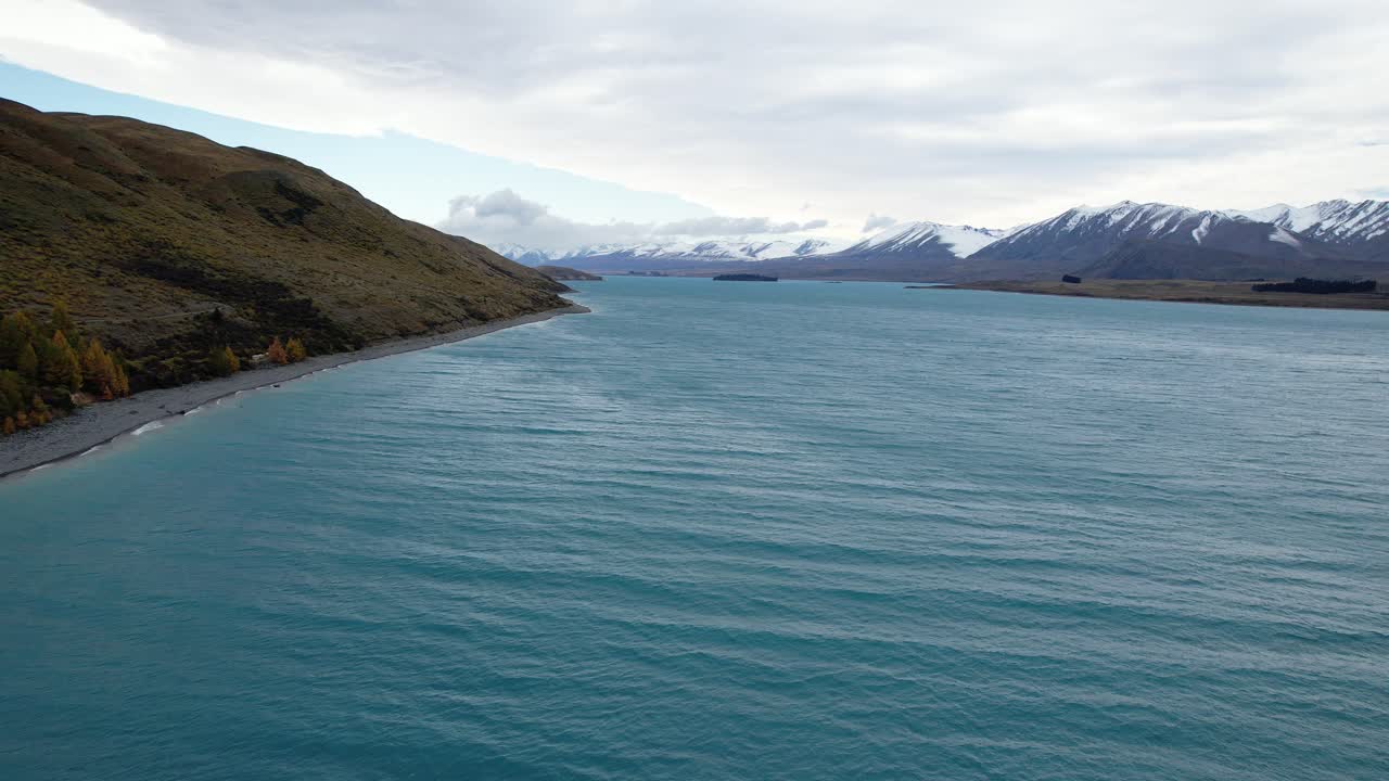 Calm Blue Water Of Lake Tekapo With Snowy Mountains In The Distance In South Island, New Zealand. - aerial shot