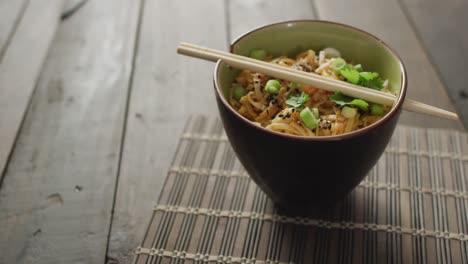 composition of bowl of pad thai with chopsticks on wooden background