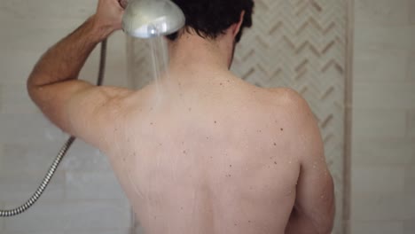 white man with dark hair washes his back with the shower head