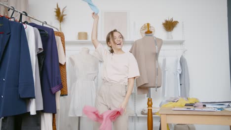 young woman fashion designer is dancing funny, waving cloth and smiling happily. self-employed woman rejoices, celebrates success of her small business