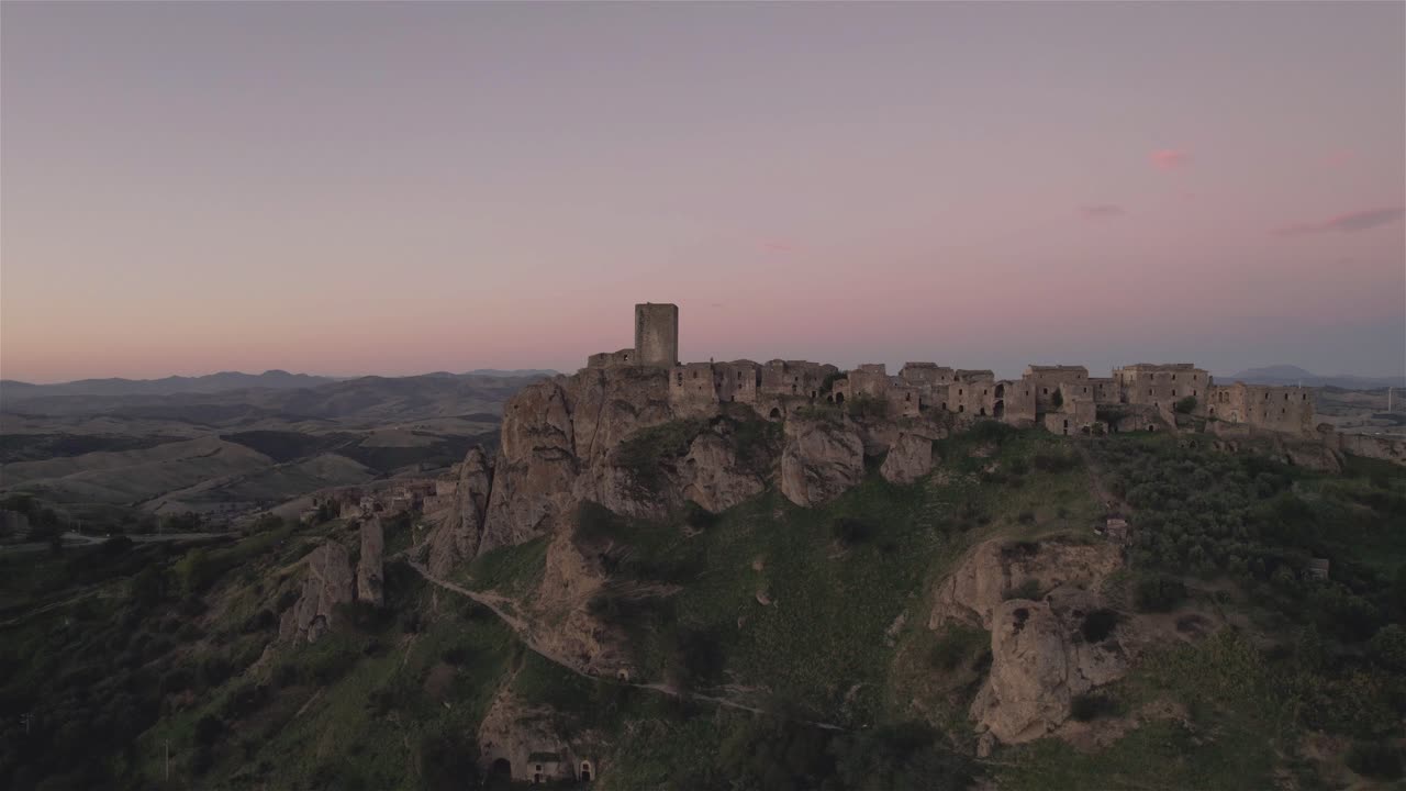 Drone flying in large circulair motion around the ruins of Craco on a hill in the south of italy finishing with the sunrise in the distance in 4k