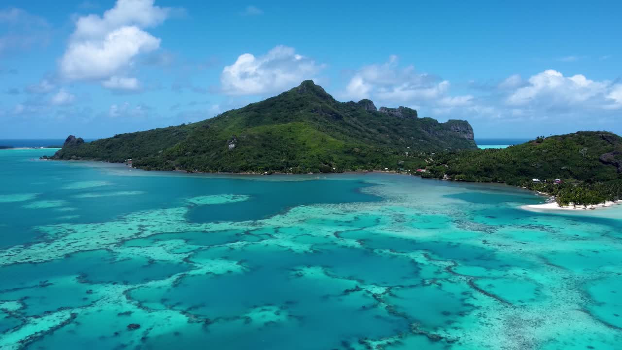 Drone view of a small green pacific tropical island with a lagoon, coral reef and blue shallow water on a sunny day in Maupiti, French Polynesia.