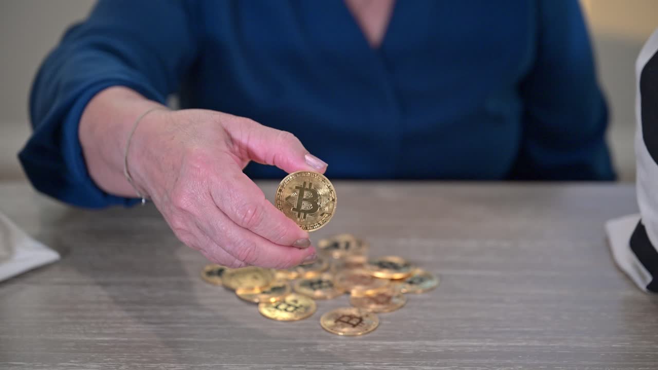 노인 여성은 토큰 비트코인을 들고 카메라에 가까이 가져와 금 기념품 토큰의 클로즈업 사진을 보여줍니다.
