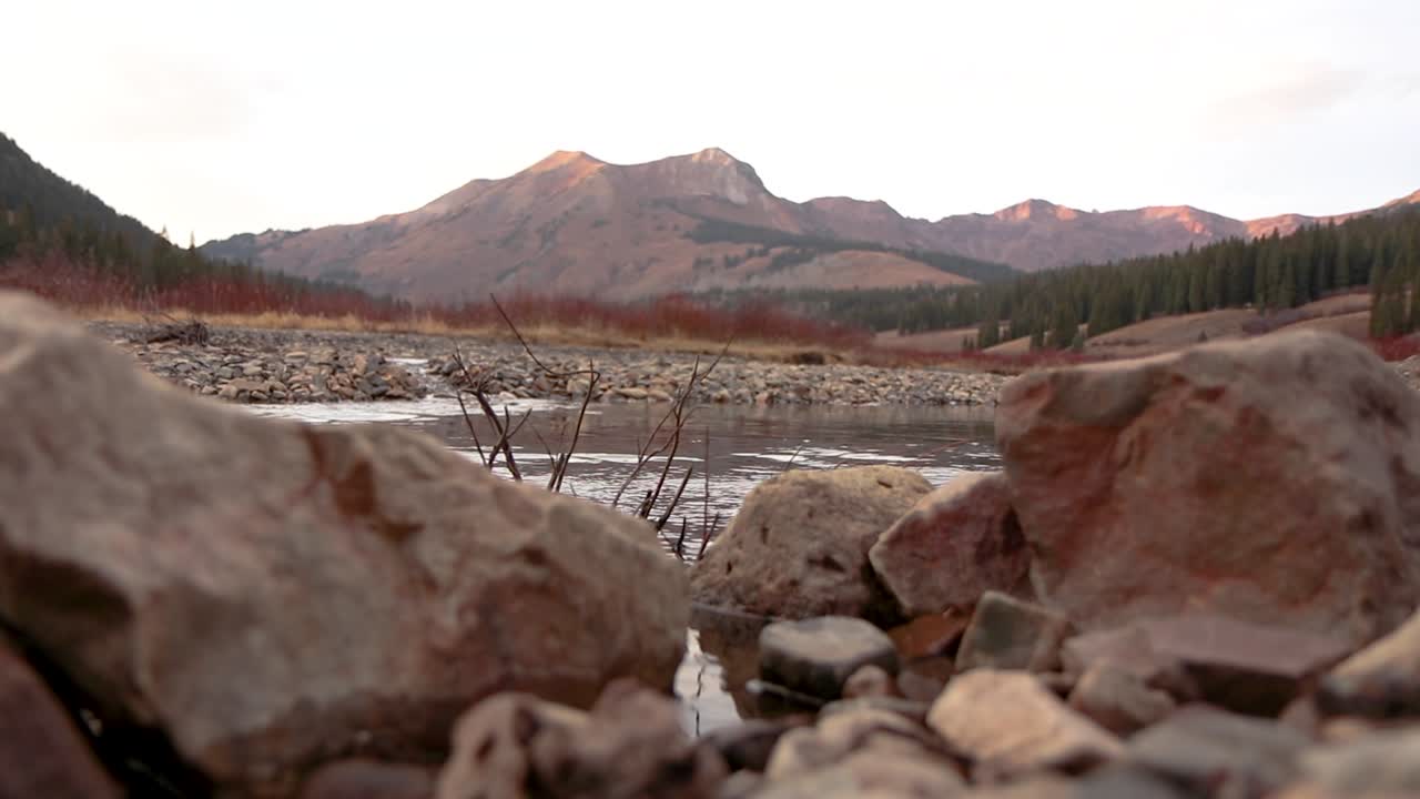Static pull focus from foreground rocks to mountain background with slow flowing river.