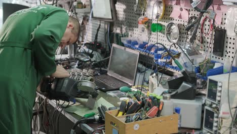 electronic equipment repair shop. the engineer technician solders the printed circuit board of an electronic device under a microscope.