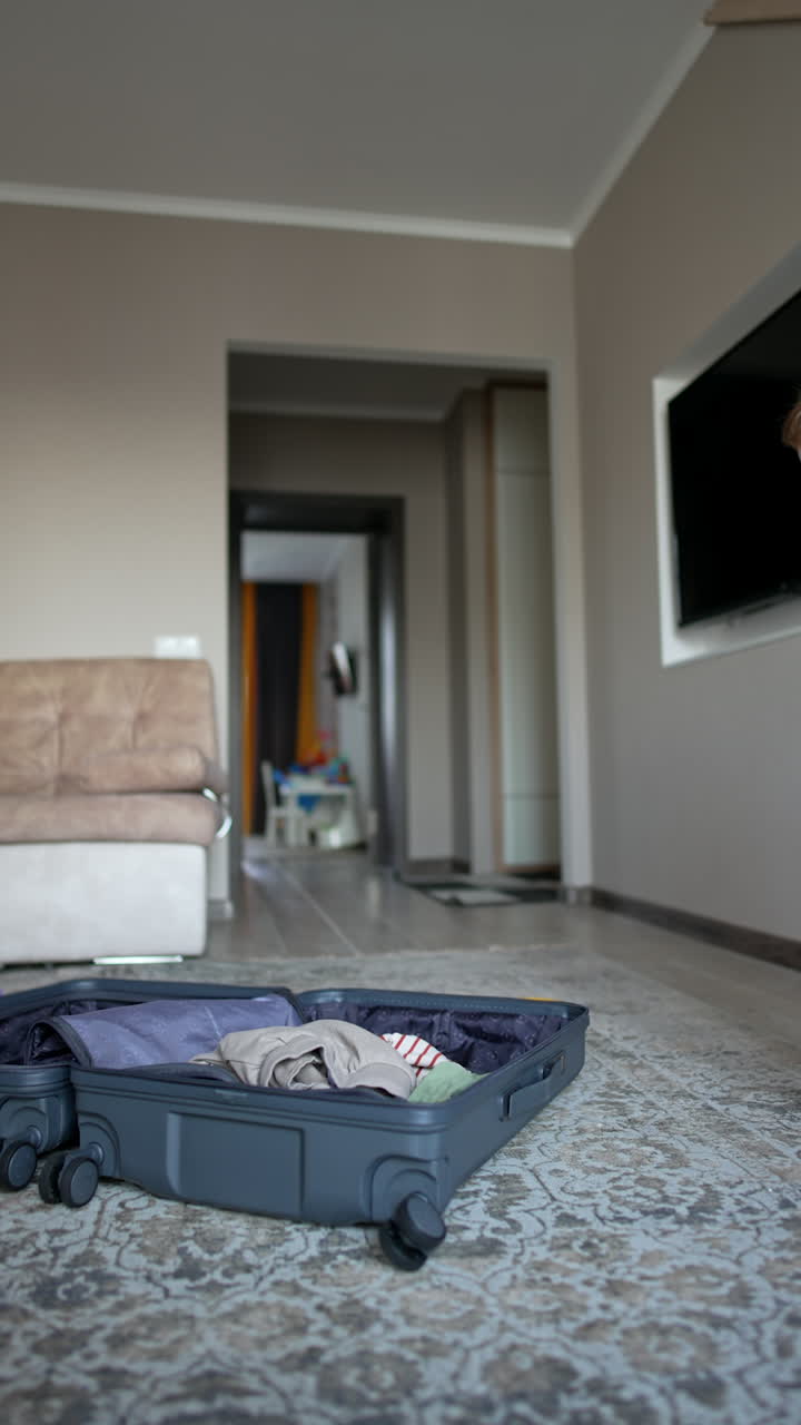 Cute toddler boy opens a big grey suitcase. Packing or unpacking clothes. Vacation concept. Vertical video.