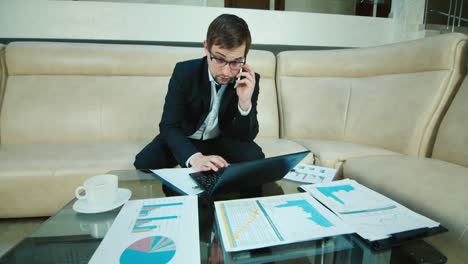 Young-businessman-working-with-documents-and-laptop-in-hotel-lobby-1