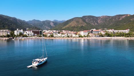 a drone flight close-up over the water surface of a boat and a beach against the backdrop of a resort town located between green hills