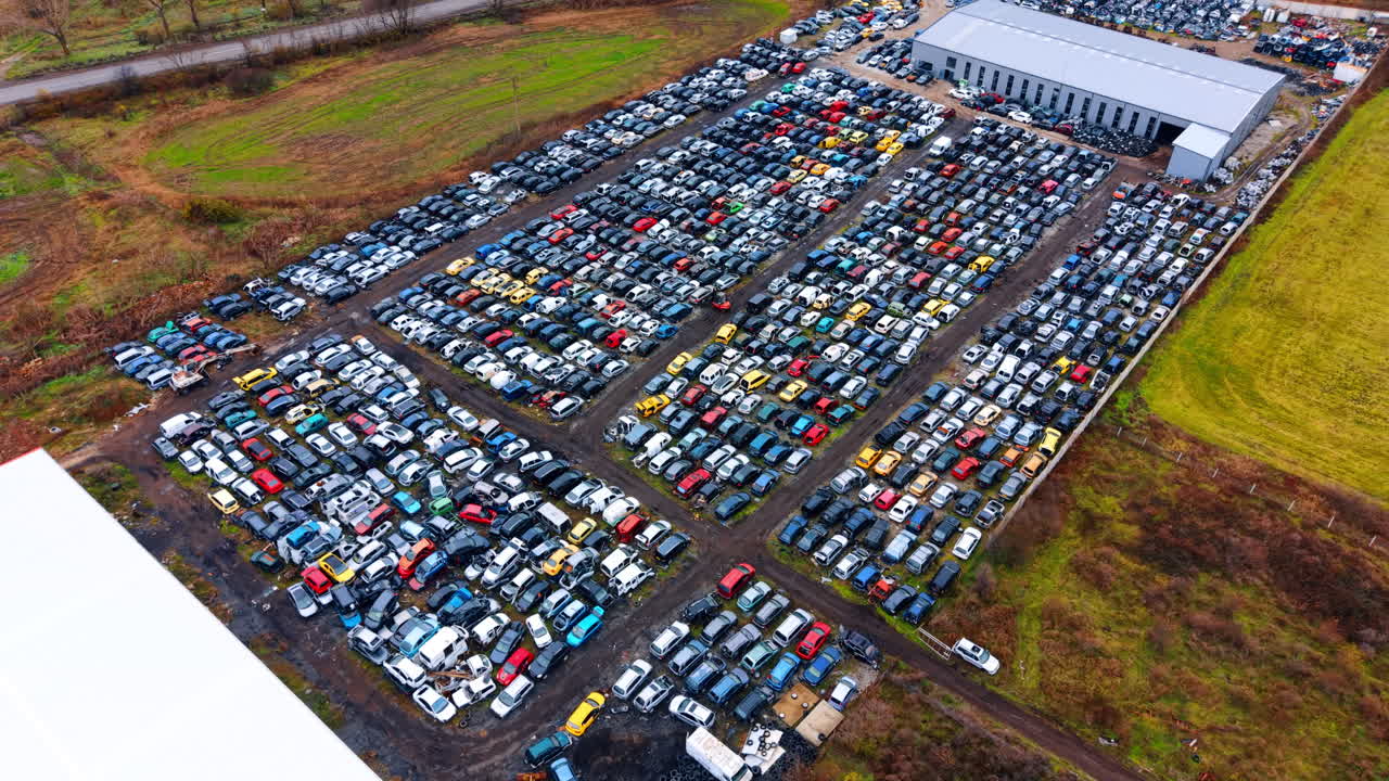 Impianto di sfasciacarrozze automobilistico su larga scala visto da drone. Ripresa aerea panoramica di un vasto lotto di riciclaggio veicoli con centinaia di auto ed edifici industriali.