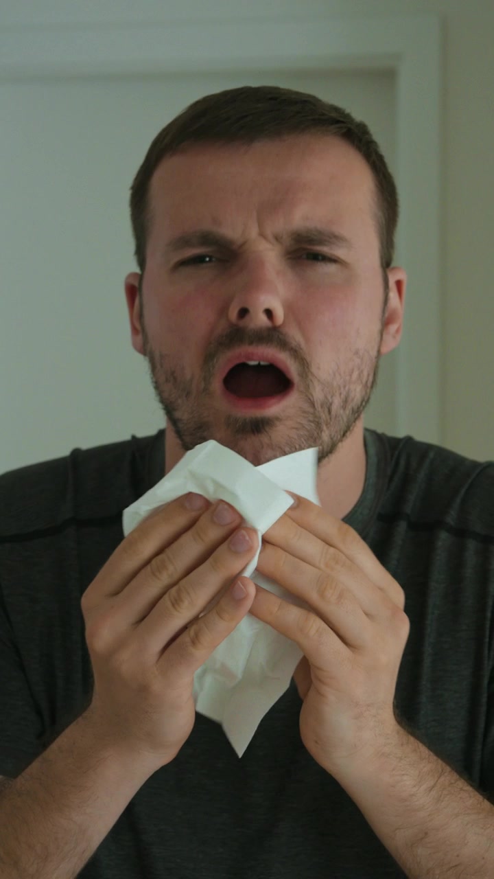 En syk mann nyser i et lommetørkle, viser forkjølelsessymptomer, influensasesong, hygiene, allergi, virusforebygging, helsevesen og hverdagssykdom hjemme