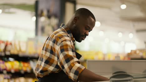 a man with black skin color in a plaid shirt inspects refrigerators in a supermarket