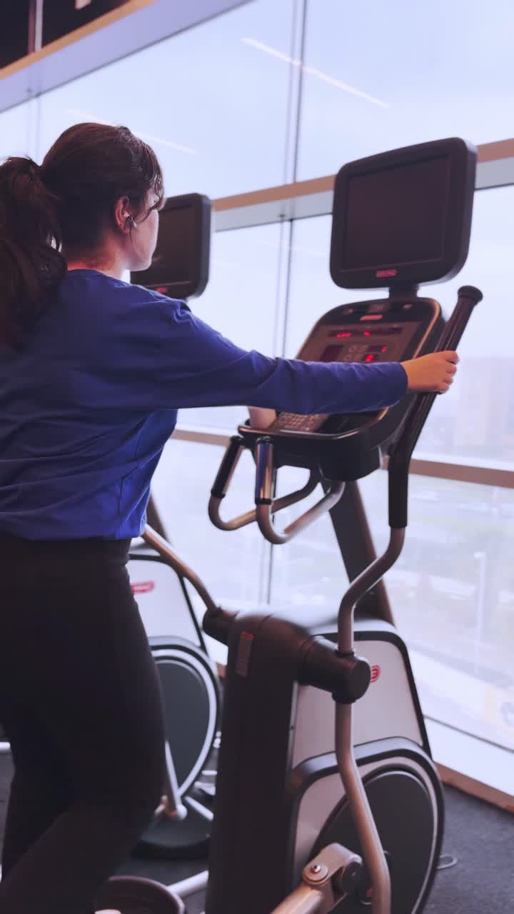 Giovane donna che si allena sull'ellittica in palestra.