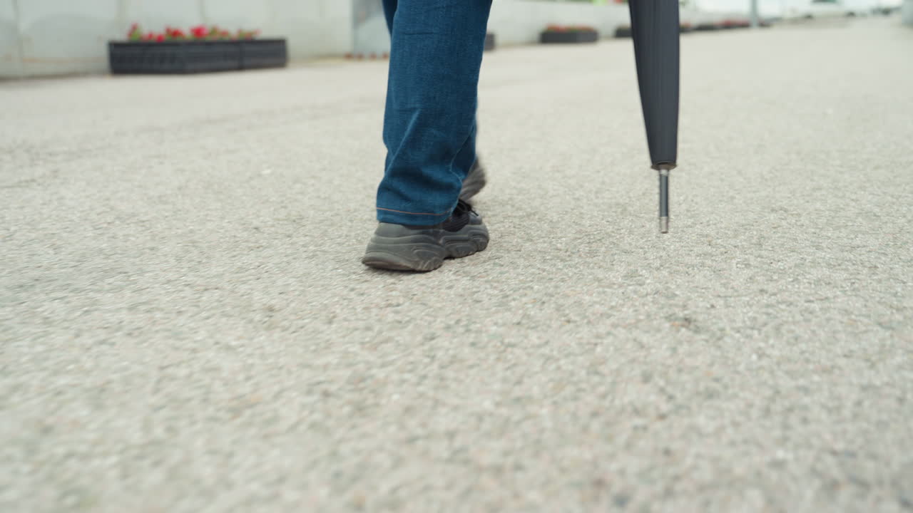 Individual traveling across urban public space. Person strides through cityscape with casual clothing and umbrella. Lone individual moves steadily through busy paved area with umbrella