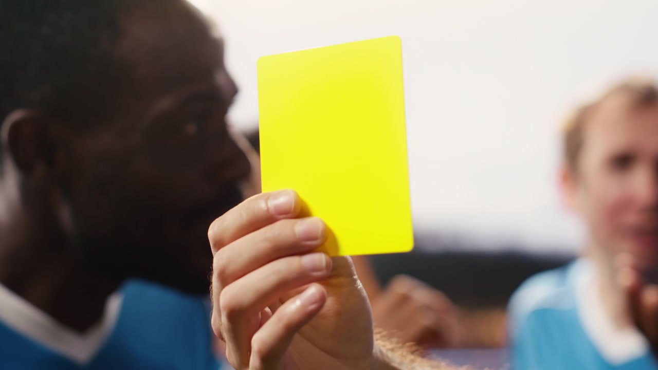 Primo piano di un cartellino giallo tenuto in mano dall'arbitro dopo una violazione delle regole durante la partita.