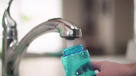 hand filling up a water bottle from a kitchen tap