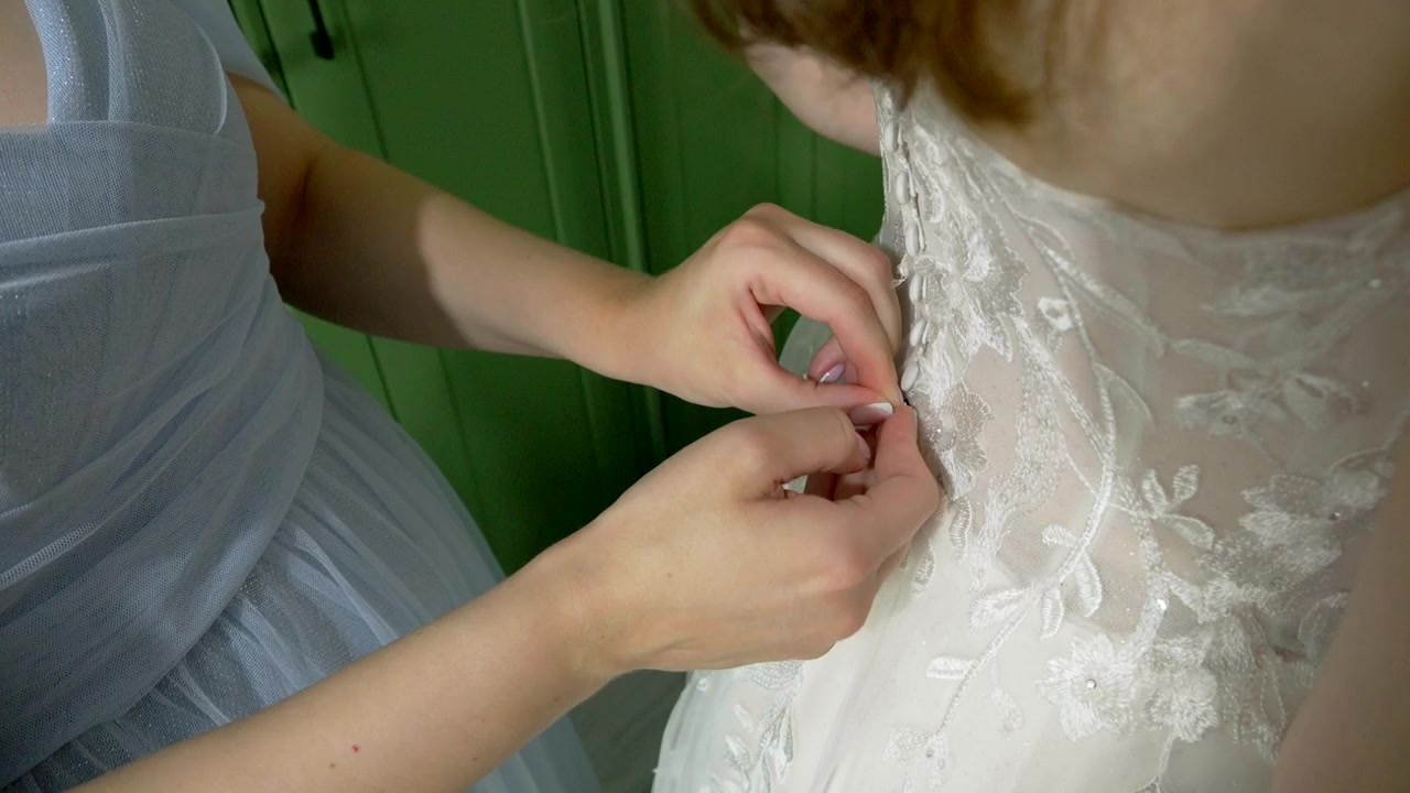 Bridesmaid helps the bride fasten her wedding dress during bridal preparations