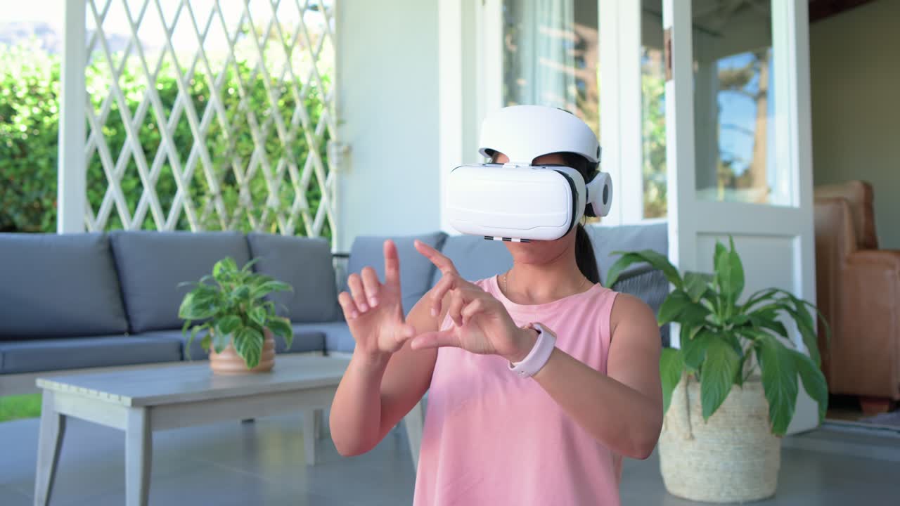 En kvinna sätter på sig ett vitt VR-headset på uteplatsen, sträcker sig och väljer kontroller för att navigera i menyn.