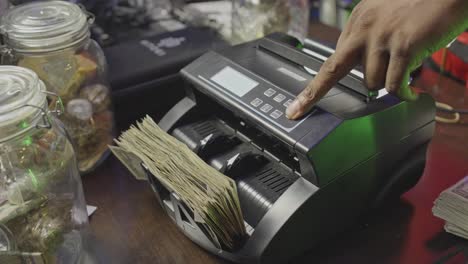 a stack of cash runs through a money counter in a studio setting, surrounded by glass jars and creative clutter — a glimpse into the hustle workflow.