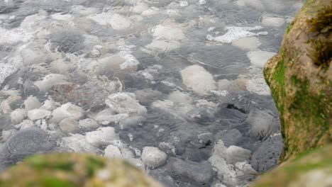 ocean waves washing over rocky pebble shoreline close up dolly right