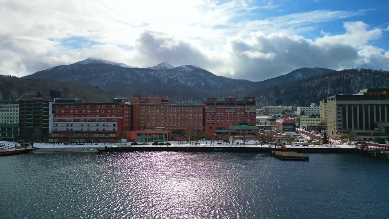 Sporingsbilde bort fra en snødekt ferieby ved innsjøen, som fremhever strålende sollys som reflekteres på det krusende vintervannet