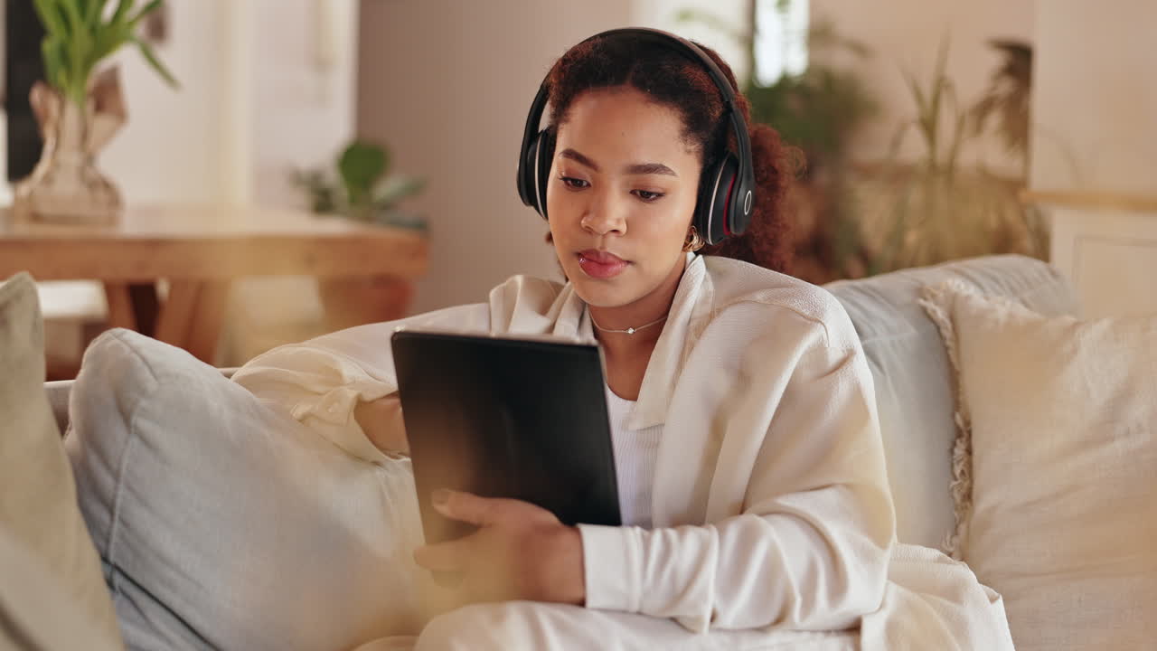 ヘッドホンとタブレットでソファでくつろぐ女性