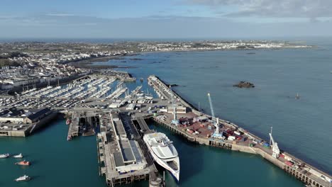 Vuelo-De-St-Peter-Port-Guernsey-Sobre-La-Terminal-De-Ferry-Con-Ferry-En-El-Muelle,-Muelle-Comercial-Con-Grúas-Hacia-La-Esquina-De-Salerie-Y-Sobre-El-Puerto-Deportivo-Qe-Ii-Con-Vistas-A-La-Bahía-De-Belle-Greve-En-Un-Día-Soleado