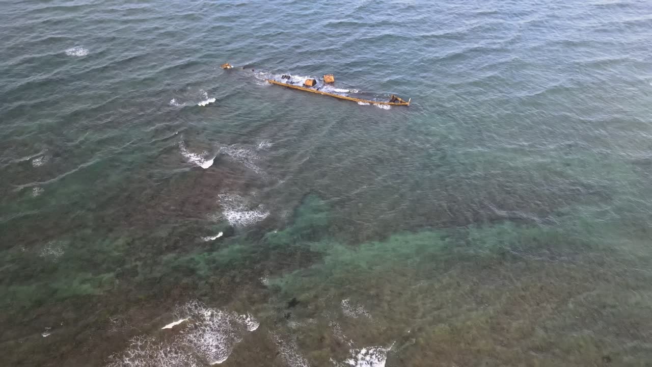 Letecký záběr dronu s klesáním na vrak lodi v oceánu, do kterého narážejí vlny.